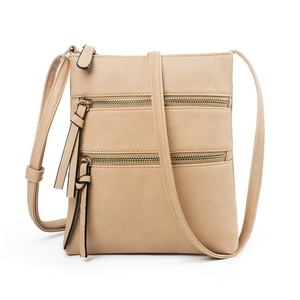 Detail of multi-pocket beige crossbody bag featuring three gold zippers and tassels