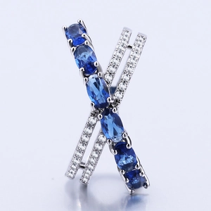 Silver X-shaped ring featuring a central blue oval gemstone and clear zircon accents