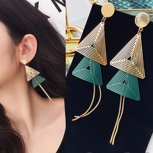 Detail showing geometric gold and green layered triangle earrings with long metal tassels