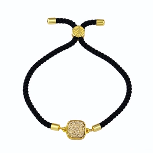 Détail d'un bracelet en corde tressée noire avec breloque carrée dorée et fermoir réglable