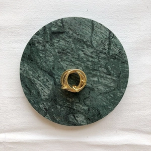 Top view of a gold multi-layer ring set on a green marble coaster and white fabric texture