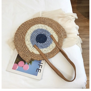 Détail d'un sac en paille tressée avec motif œil bleu et poignées en similicuir