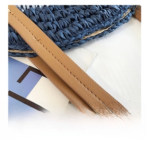 Détail de la couture précise sur la poignée en cuir marron du sac en paille tressée bleu