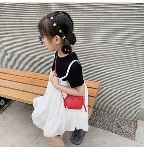 Close-up of a cute red pig-shaped kids crossbody bag worn by a little girl on a wooden bench
