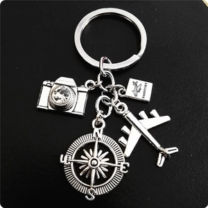 Travel keychain with silver metal airplane, camera, compass and passport charms on black leather