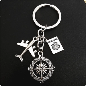 Detail of travel keychain featuring silver airplane, passport tag, and compass charm
