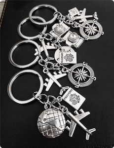 Detailed silver metal keychain featuring airplane, passport, compass, and globe charms