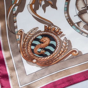 Macro detail of nautical silk scarf featuring heraldic crest prints and magenta borders