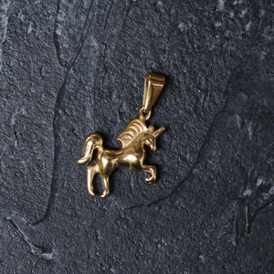 Minimalist gold-plated stainless steel unicorn pendant on a textured dark stone background