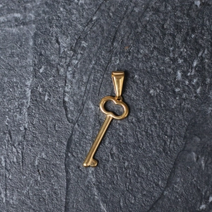 Detailed view of a polished gold-plated key pendant on a dark grey stone surface