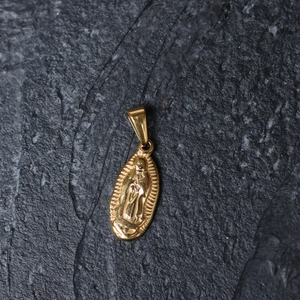 Detail of gold-plated oval Virgin Mary pendant on dark textured stone surface