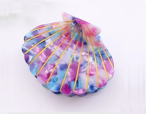 Macro detail of seashell-shaped hair claw with iridescent acetate and golden ridges