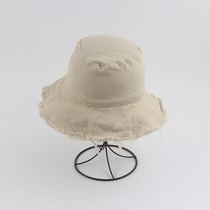 Detail shot of beige distressed cotton bucket hat with raw frayed edges on a metal stand