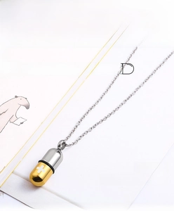 Macro view of polished two-tone capsule pendant with cross detail on stainless steel chain