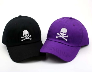 Detail view of black and purple cotton baseball caps featuring white skull embroidery