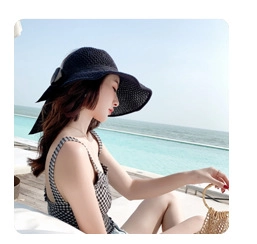 Close-up of a black straw sun hat with a large bow detail by a seaside swimming pool