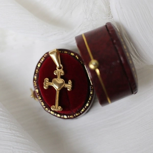 Close-up of a gold cross pendant with heart center in a red vintage jewelry box