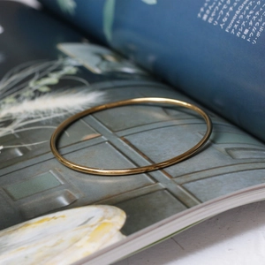 Minimalist 18K gold plated thin wire bangle shown on a magazine and natural grass
