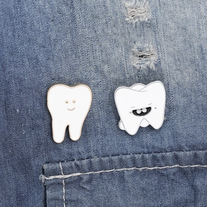 Cartoon tooth enamel pin set with white finish and gold trim on denim fabric