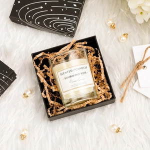 Top view of white scented candle in glass cup with elegant black gift box on plush rug