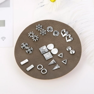 Detail shot of silver alloy earring set with geometric and floral patterns on leather mat