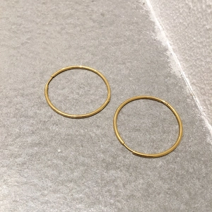 Detailed close-up of polished gold-plated stainless steel hoop earrings on a textured background