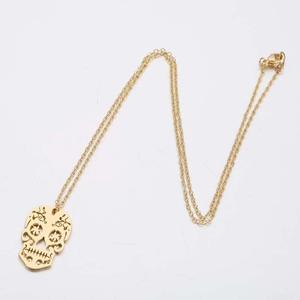 Detail of gold skull pendant necklace with intricate patterns on a delicate fine chain