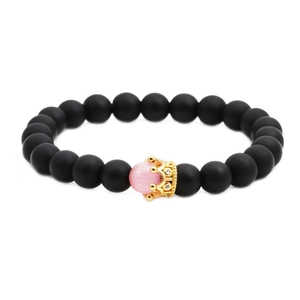 Detailed close-up of matte black beads and golden crown charm with a pink opal center