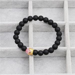 Detail of matte black beads bracelet with golden crown and pink accent in a jewelry box