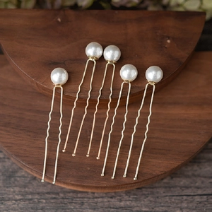 Detailed view of pearl U-shaped hair pins with gold metal finish on a wooden stand