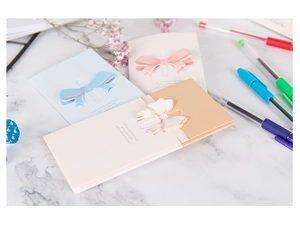 Detail of 3D bow cards in pastel colors with pens and dried flowers on marble surface