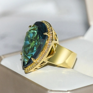 Macro shot of a teardrop-shaped teal crystal ring with diamond accents in a beige box