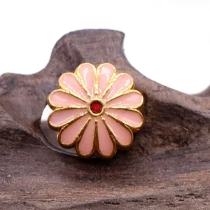 Close-up of pink enamel sunflower pendant with gold metal edges on a wooden base