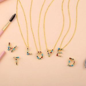Detail of colorful zircon letter pendants on gold necklaces with brush accessory