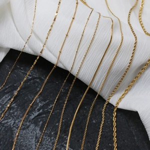 Detailed view of nine gold-plated titanium steel chain styles on a black rock surface