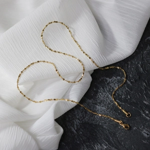 Detailed shot of golden flat disc chain necklace with lobster clasp on texture background