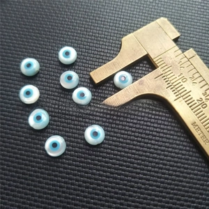 Macro shot of evil eye mother of pearl beads with brass caliper measuring diameter
