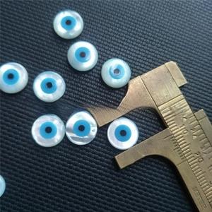 Macro shot of a 10mm evil eye shell bead being measured with a brass caliper tool