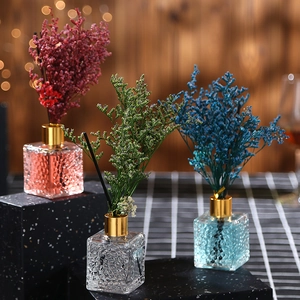 Three square glass reed diffusers with red, green, and blue dried flower decorations