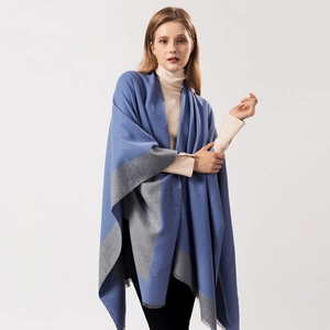 Detail of blue and grey knit shawl with fringed edges on a model in a studio setting