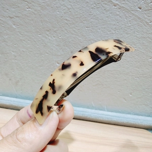 Detailed macro view of a leopard print spring hair clip held against a textured wall