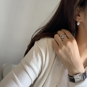 Detail view of woven silver ring paired with pearl earrings and a classic leather watch