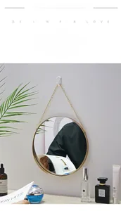 Close-up of a Nordic round mirror with golden metal frame and chain hanging on a white wall