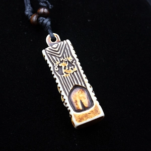 Macro shot of a bone-like Tiki pendant with dark brown totem carvings and black cord