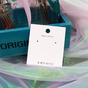 Close-up of a white rectangular earring display card on a soft decorative background