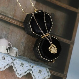 Detail of gold Monstera leaf pendant on fine chain inside a black jewelry box