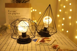 Close-up of geometric metal frame table lamps with warm LED string bulbs and black finish