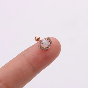 Macro d'un clou d'oreille en or rose avec opale et diamants sur le bout d'un doigt