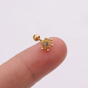 Vue macro de la boucle d'oreille soleil dorée avec zircon et fermoir à vis sur un doigt