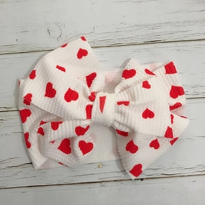 Detail of baby headband with large bow and red heart pattern on white textured fabric